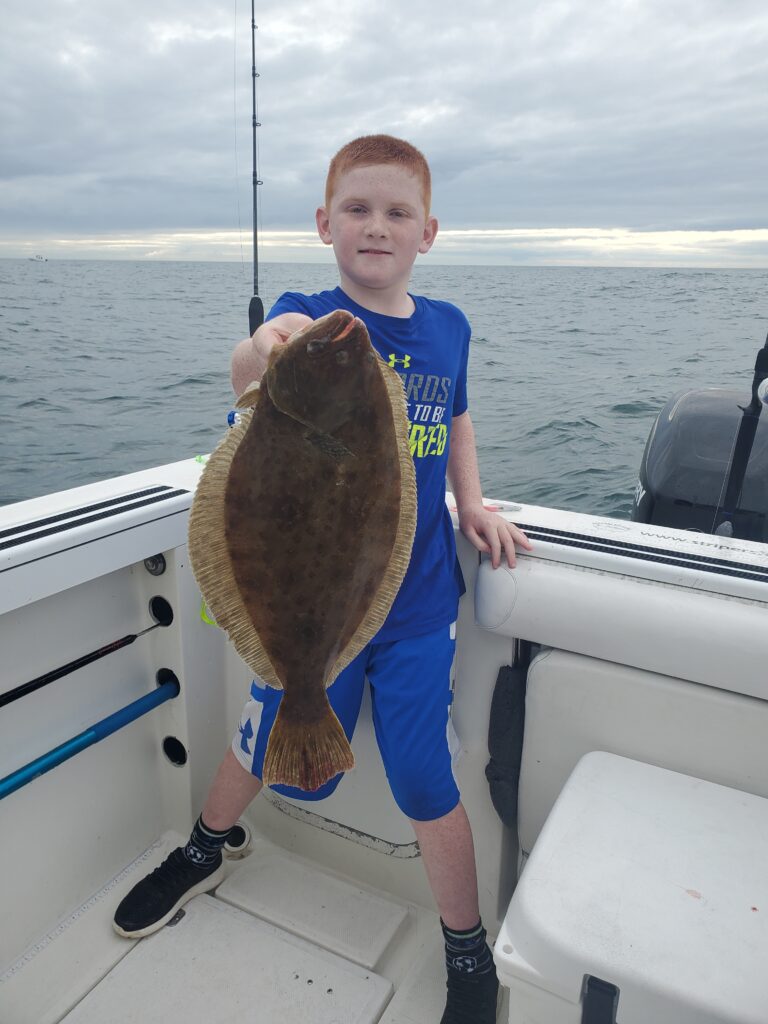 Young boy on a boat holding a freshly caught Fluke during a saltwater fishing trip